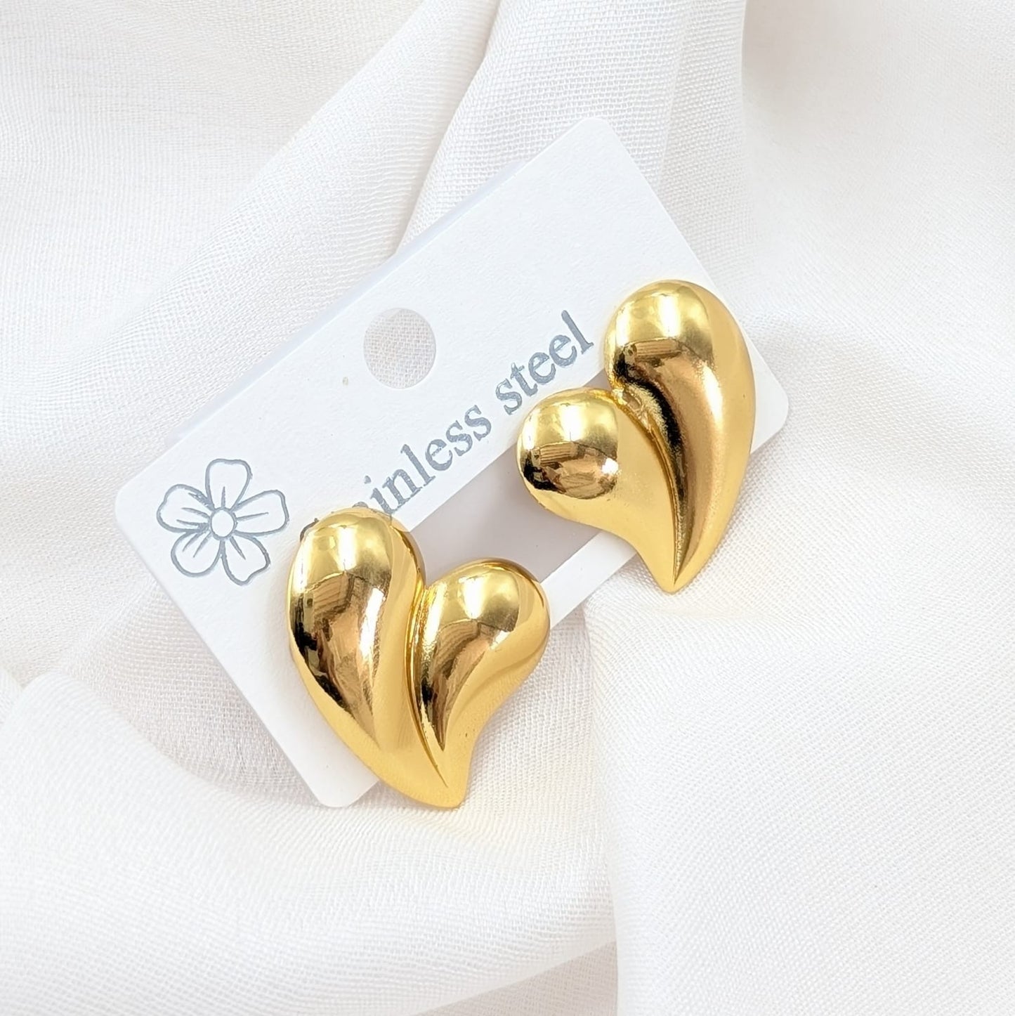 Gold heart-shaped earrings on a white card with 'ainless steel' text.