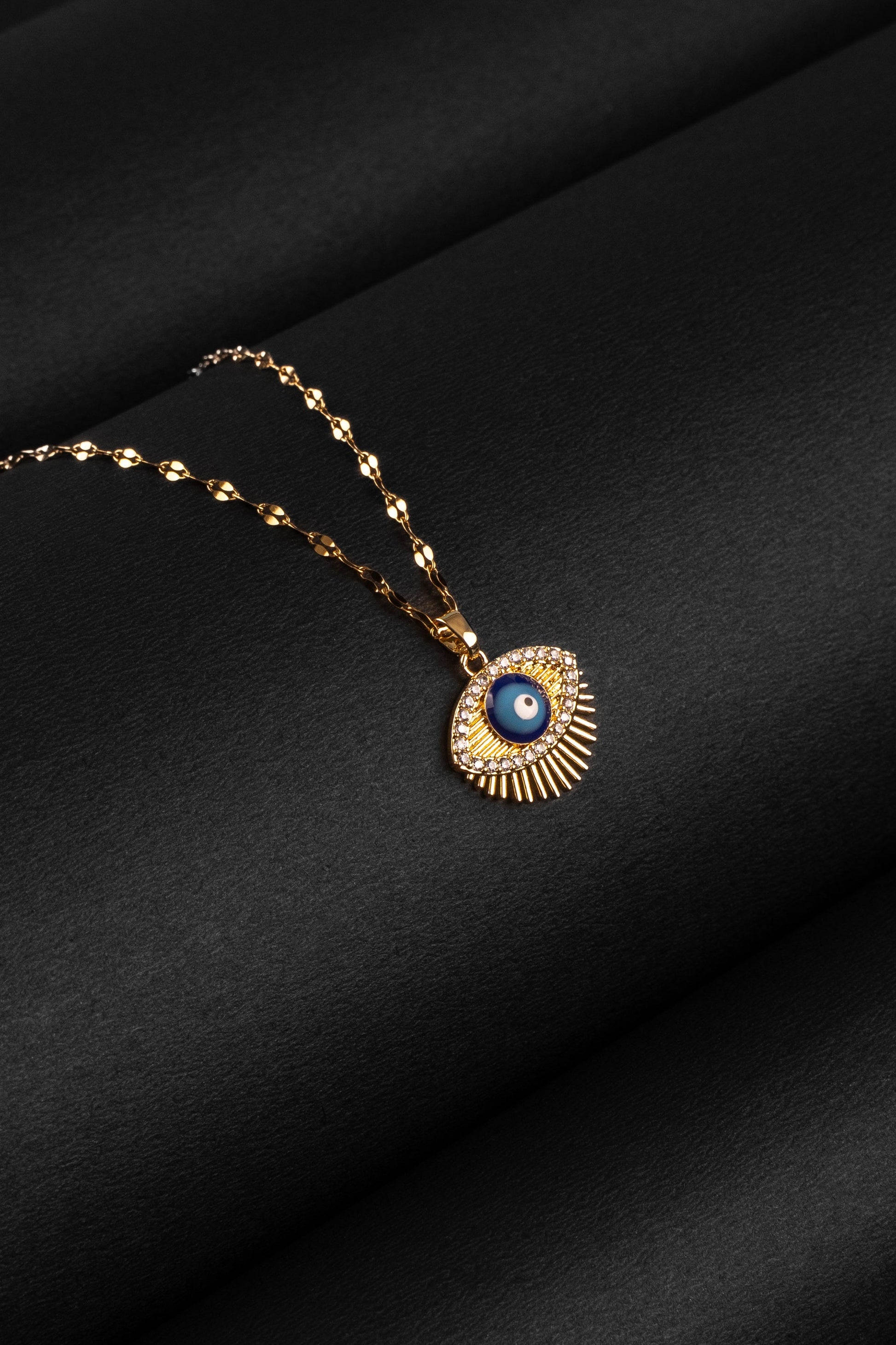 Gold necklace with a evil eye pendant on a black fabric background