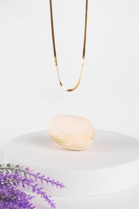 Gold necklace on a white plate with a bar of soap and lavender sprigs.