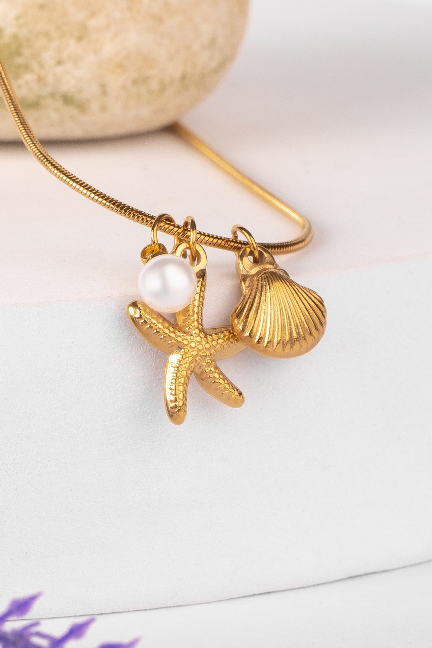 Gold necklace with starfish, shell, and pearl pendant on a white background