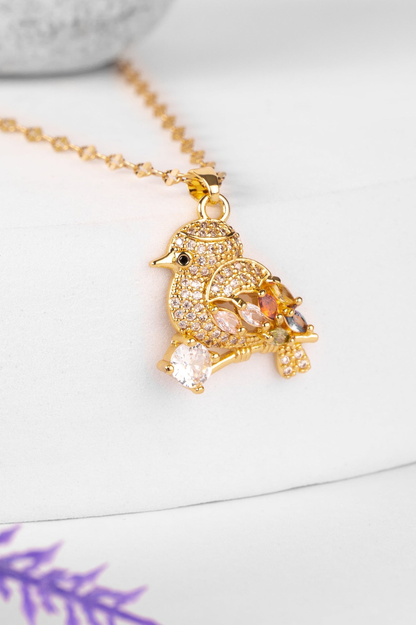 Gold necklace with a detailed pendant on a white surface bird with stud 