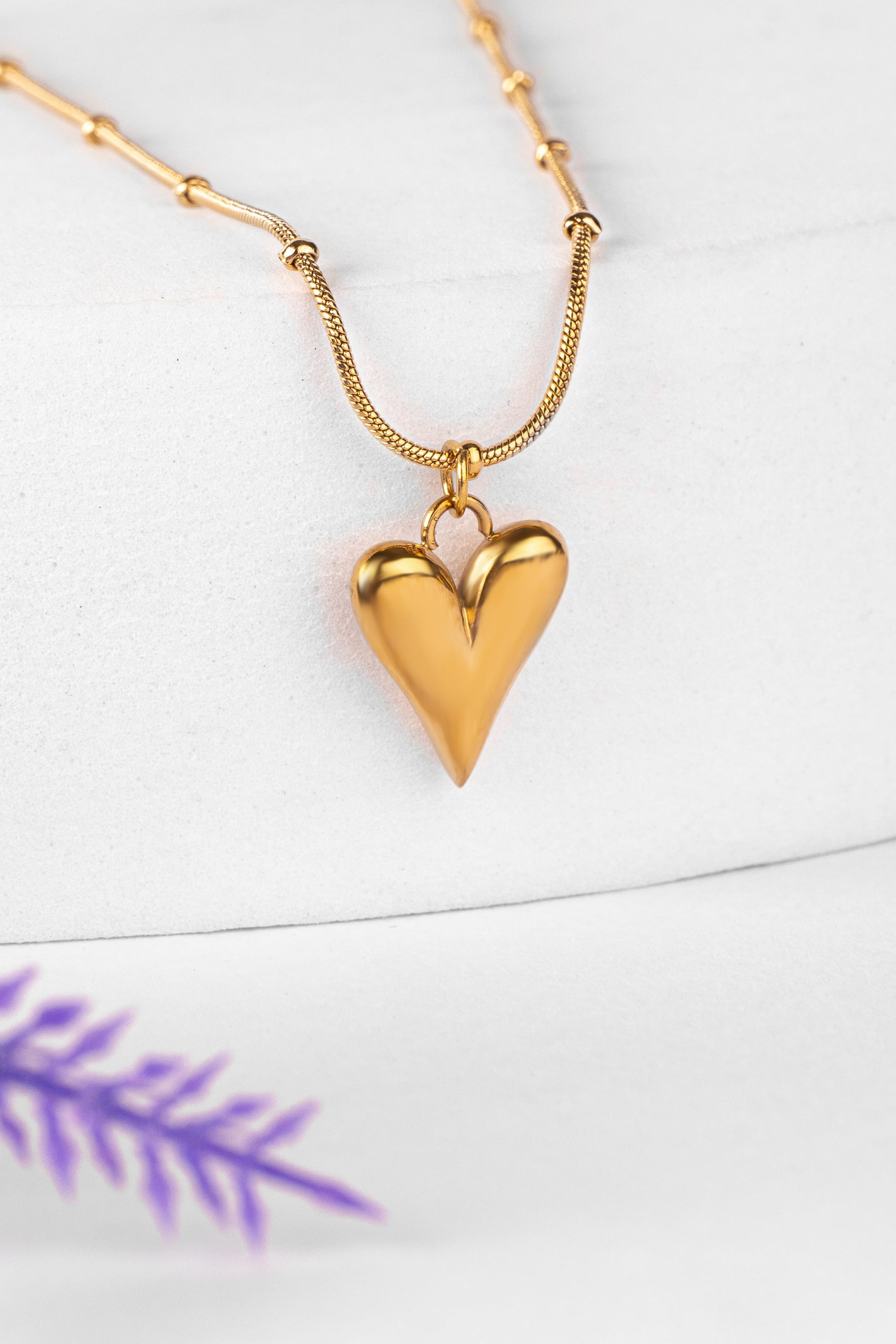 Gold heart-shaped pendant necklace on a white background with purple leaf design