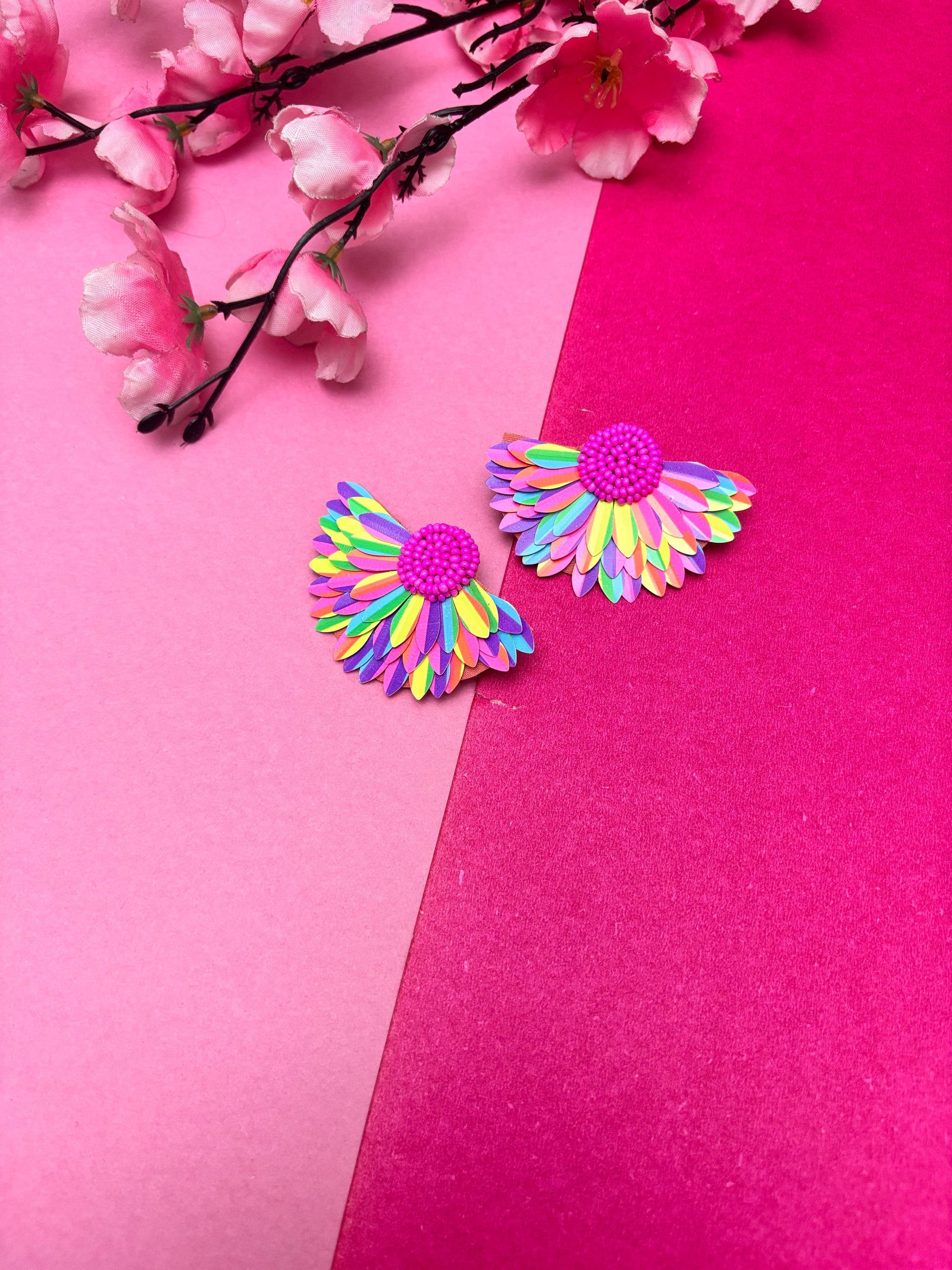 Colorful flower-shaped earrings on a pink background with cherry blossoms.