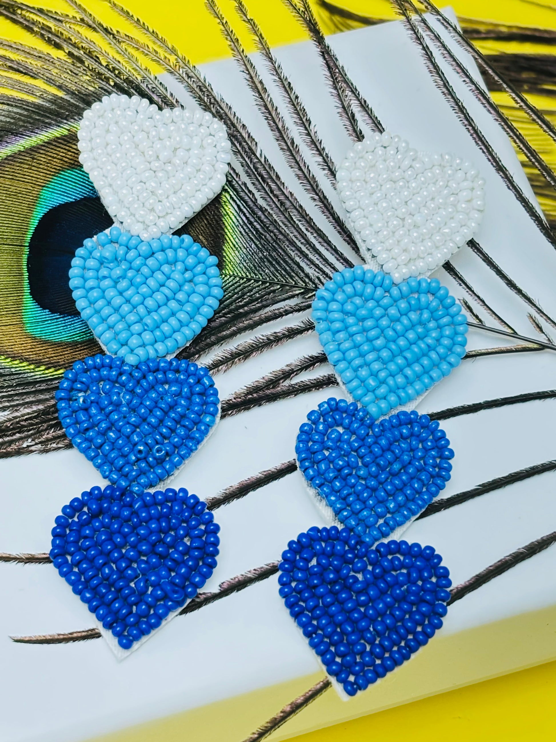 Pair of beaded heart-shaped earrings on a peacock feather background