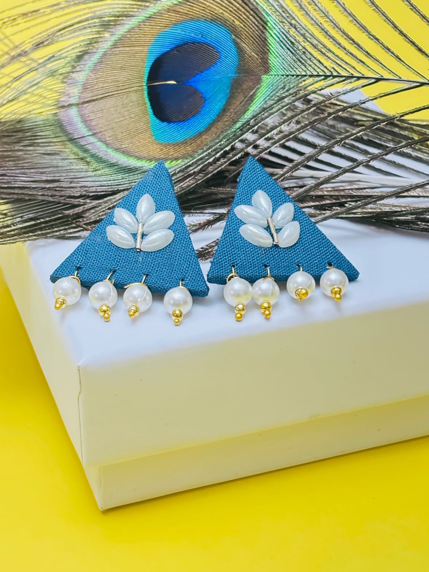 Triangular earrings with pearl details on a peacock feather background