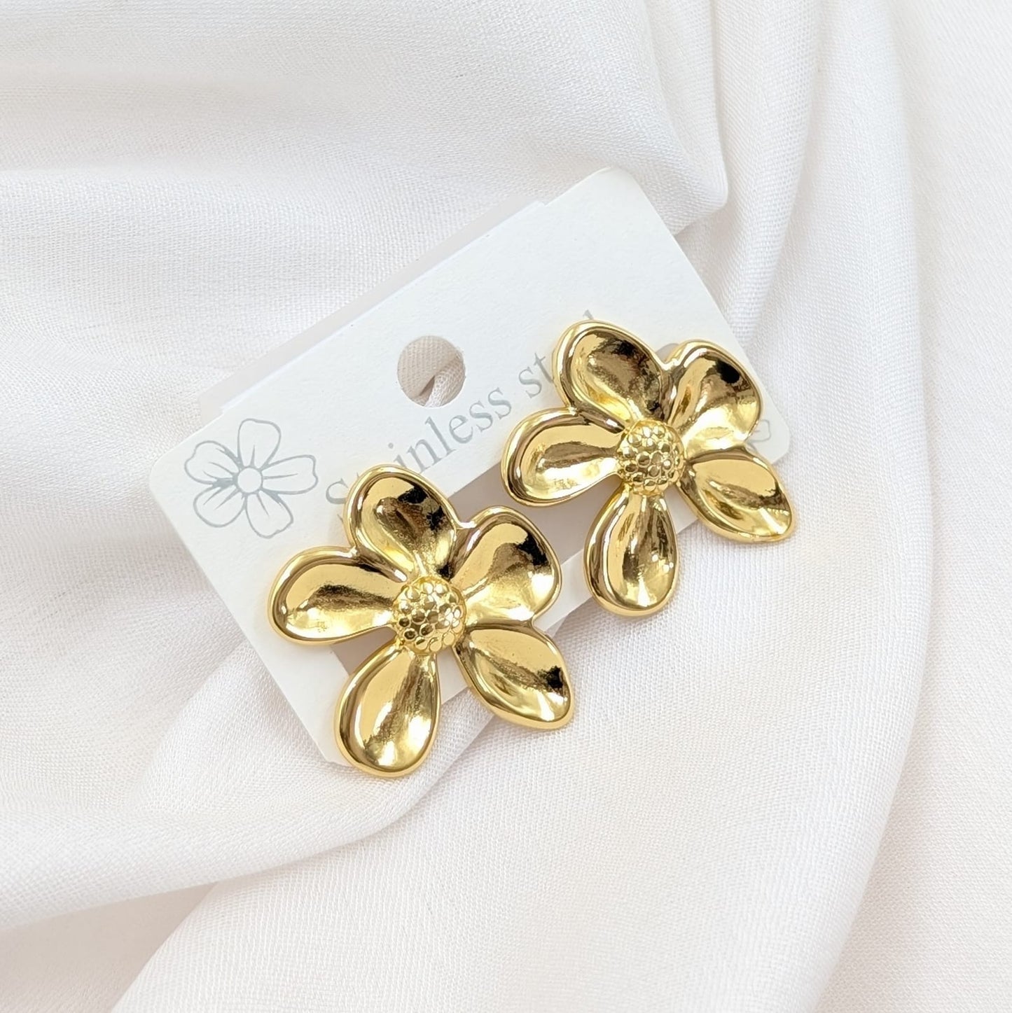 Gold flower-shaped earrings on a white card with a white background