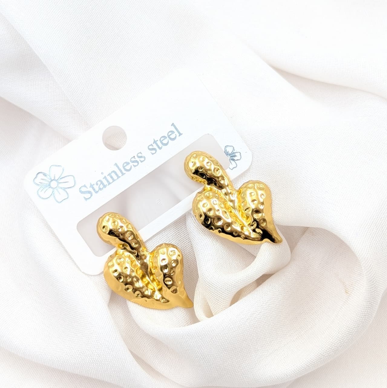 Gold leaf-shaped earrings on a white card with 'Stainless steel' text, displayed on a white background.