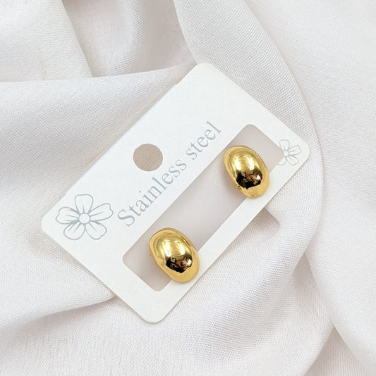 Gold earrings on a white card with 'Stainless steel' text, placed on a white fabric background.